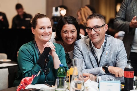 Three delegates smiling at their table at the Māori Leadership Summit 2025