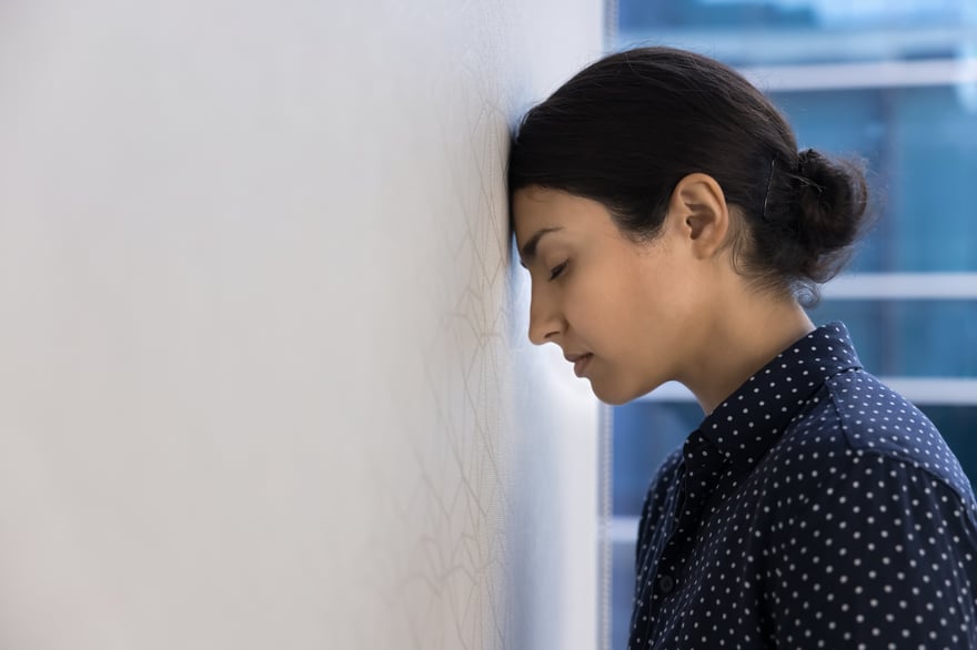A professional pausing with her forehead against a wall, eyes closed, capturing the weight of unmanaged workplace pressure