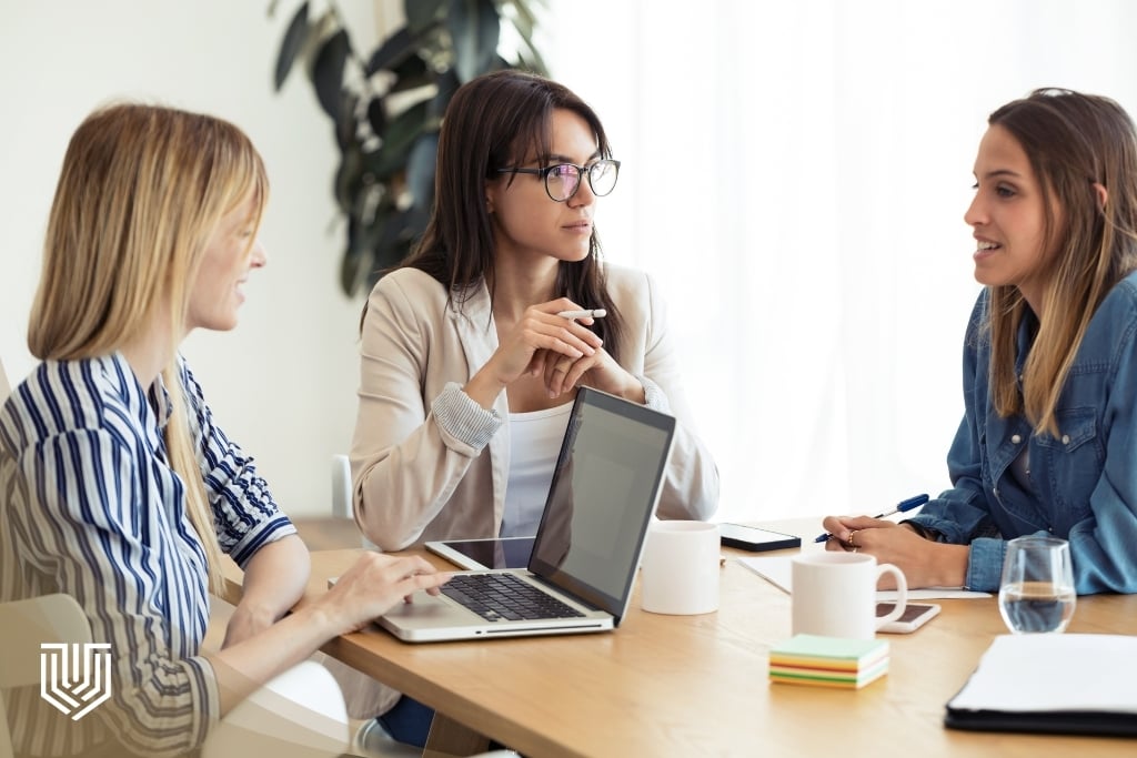 Three professionals collaborating around a table with laptops and coffee