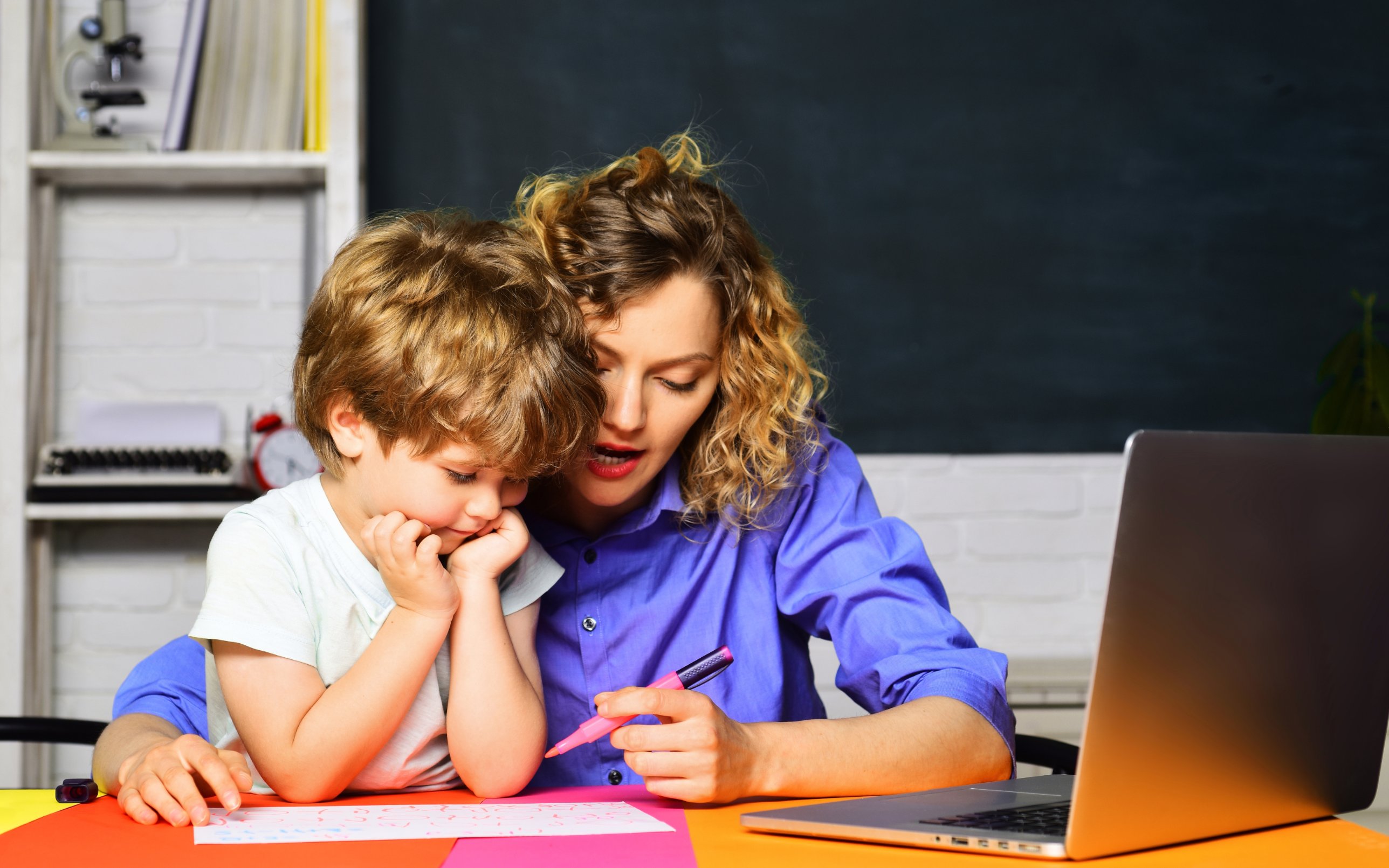 A teacher sitting beside a young student, working through his writing together