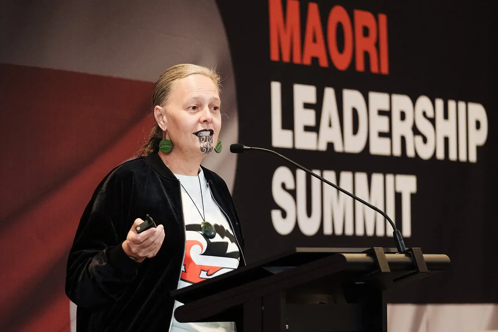 A speaker with moko kauae presenting at the Māori Leadership Summit 2025